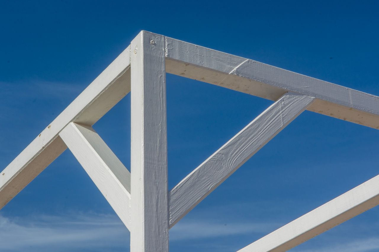 Minimalist view of a white wooden structure with blue sky background, highlighting geometric design.